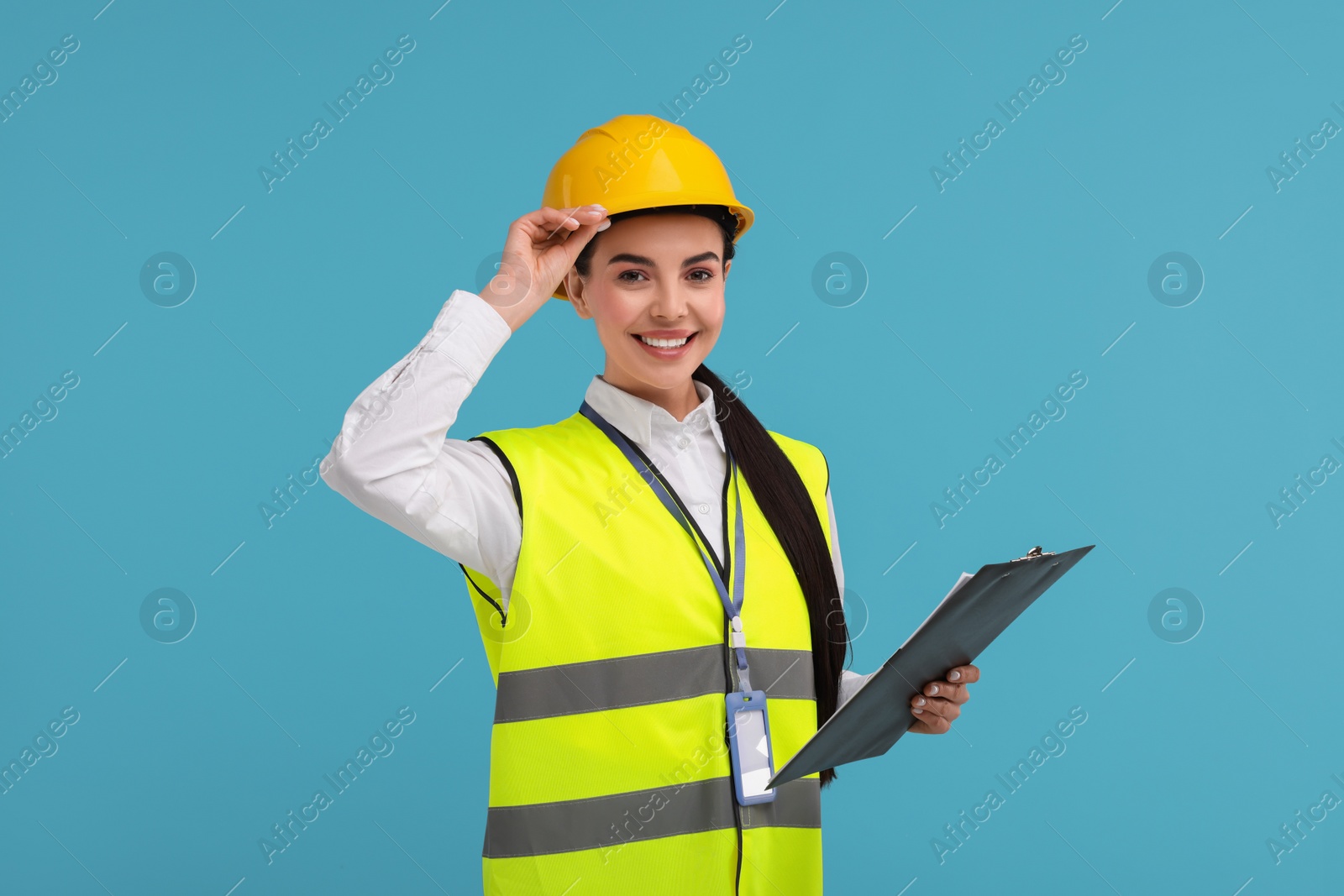 Photo of Engineer in hard hat holding clipboard on light blue background