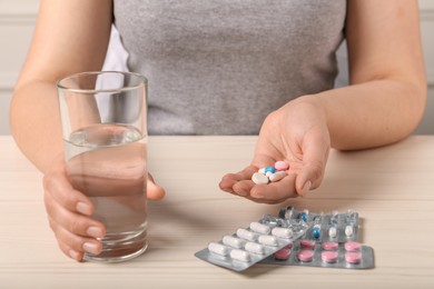 Woman with different pills and glass of water at white wooden table, closeup