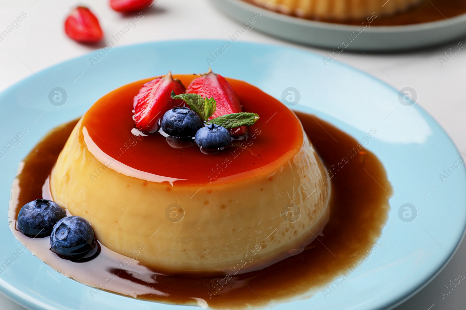 Photo of Delicious pudding with caramel, strawberries and blueberries on white table, closeup