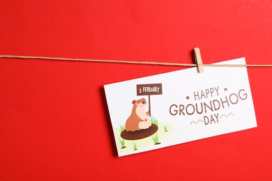 Photo of Happy Groundhog Day greeting card hanging on red background, space for text
