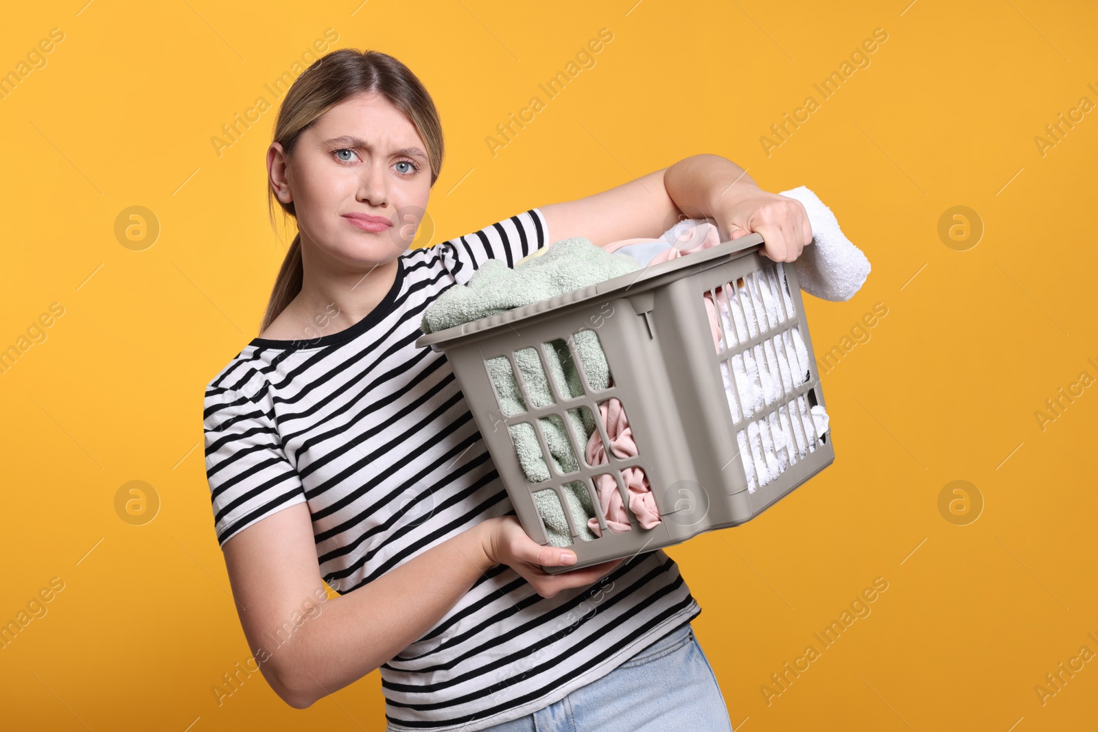 Photo of Sad woman with basket full of laundry on orange background