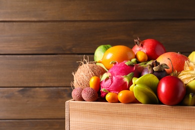 Crate with different exotic fruits on wooden background. Space for text