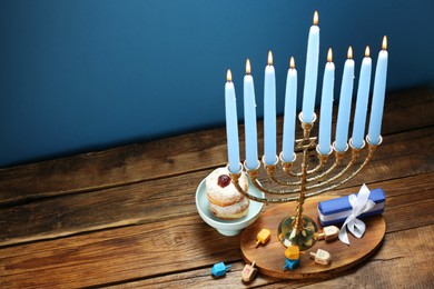 Hanukkah celebration. Menorah with burning candles, dreidels, donuts and gift box on wooden table, above view. Space for text