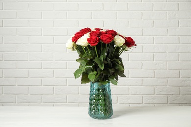 Luxury bouquet of fresh roses on table near white brick wall