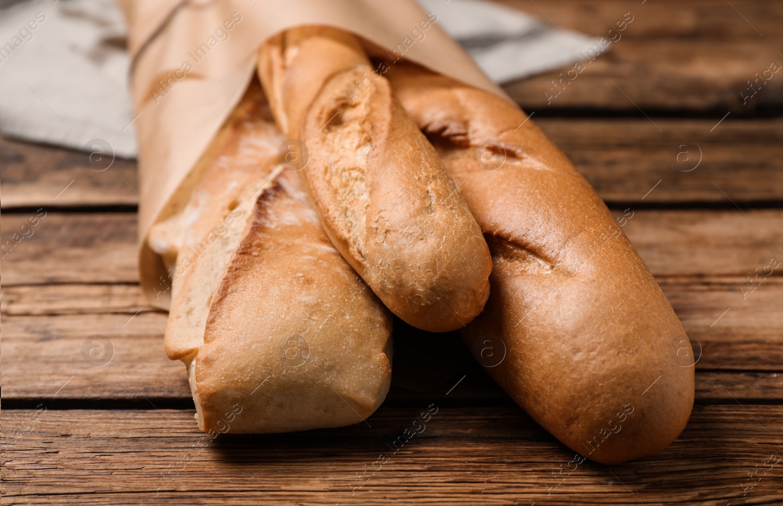 Photo of Fresh tasty baguettes in package on wooden table, closeup