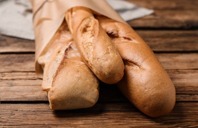 Photo of Fresh tasty baguettes in package on wooden table, closeup