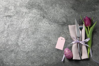 Photo of Cutlery set, painted egg and beautiful flower on grey table, flat lay with space for text. Easter celebration