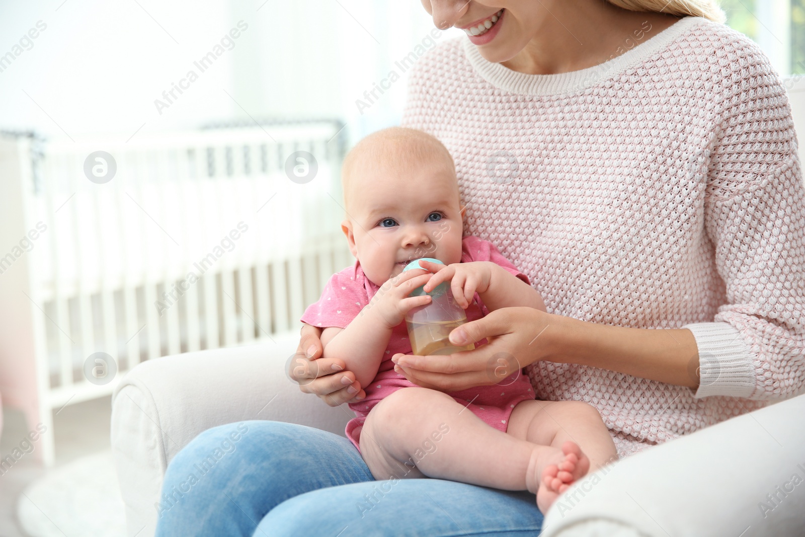 Photo of Lovely mother giving her baby drink from bottle in room