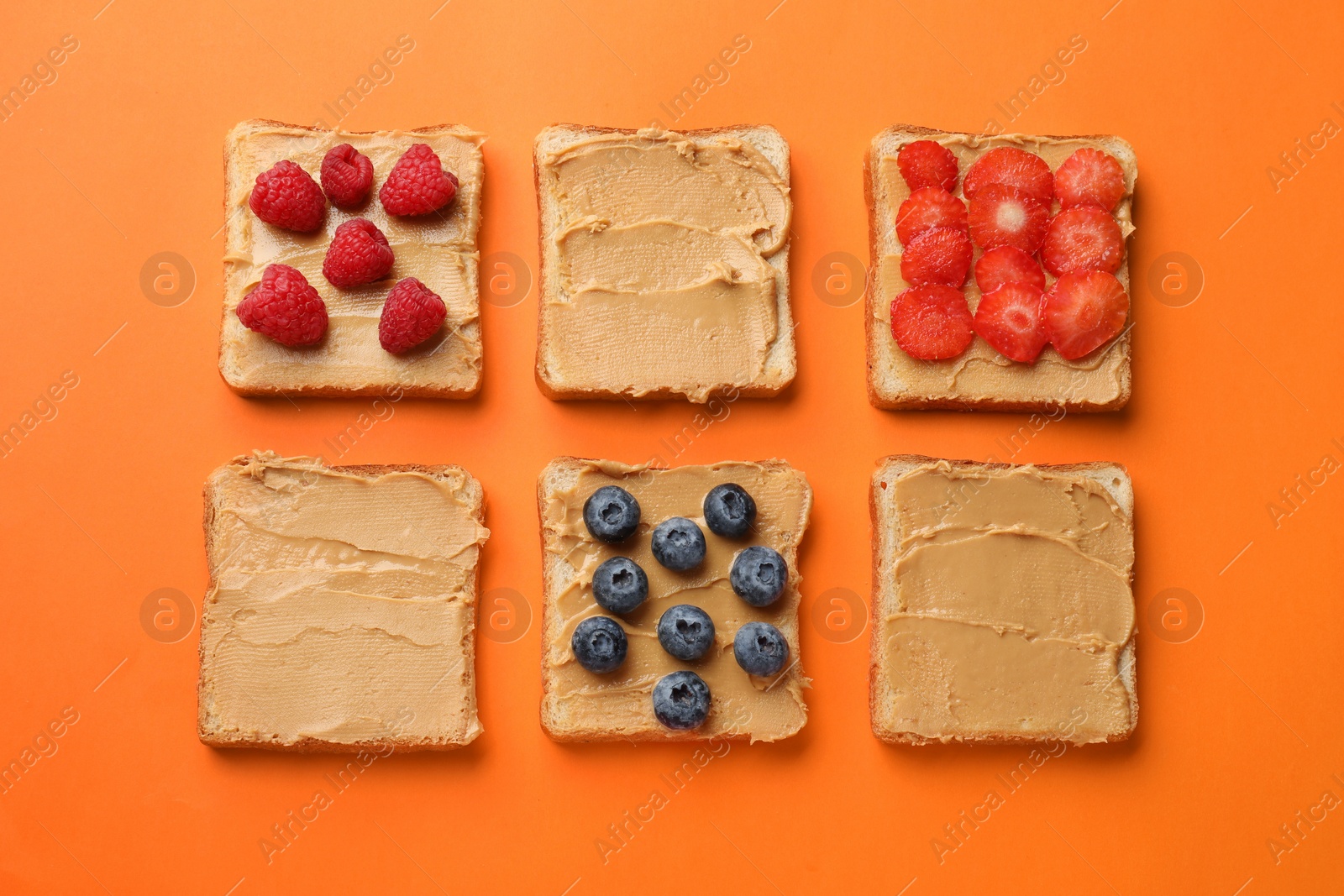 Photo of Tasty peanut butter sandwiches with fresh berries on orange background, flat lay