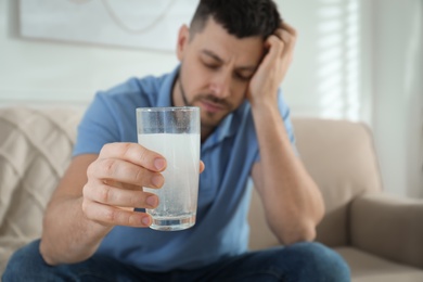 Photo of Man taking medicine for hangover at home, focus on hand with glass