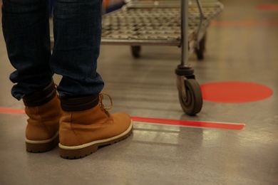 Person with shopping cart standing behind taped floor marking in store for social distance, closeup. Preventive measure during coronavirus pandemic