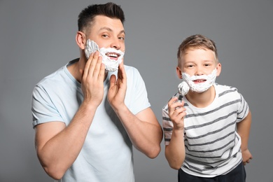 Dad and son applying shaving foam on grey background
