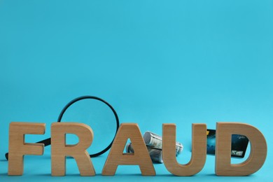 Word Fraud made of wooden letters near money, credit card and magnifying glass on light blue background, space for text