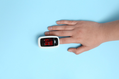 Photo of Woman using modern fingertip pulse oximeter on light blue background, top view