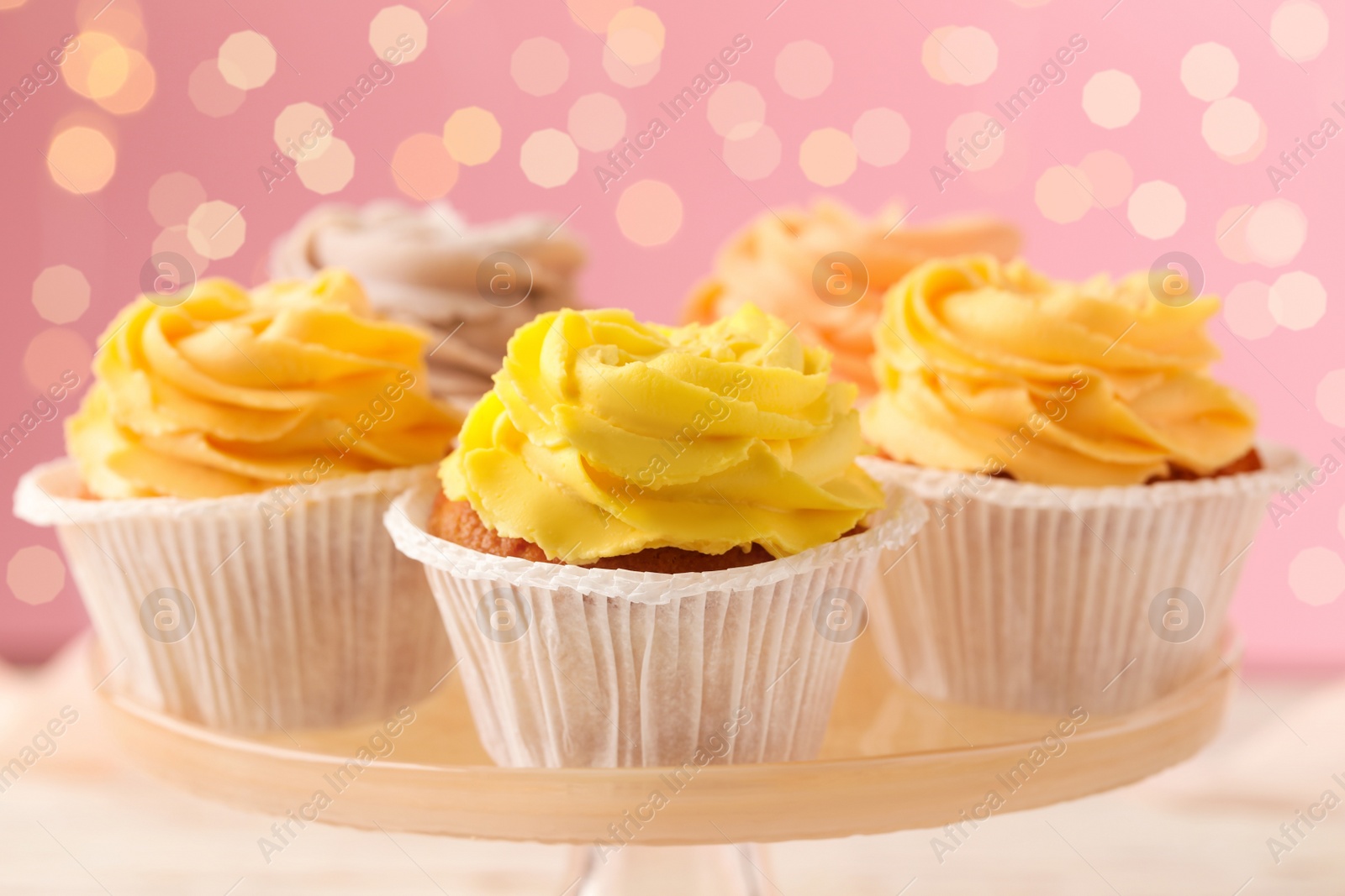 Photo of Stand with tasty cupcakes against blurred lights, closeup