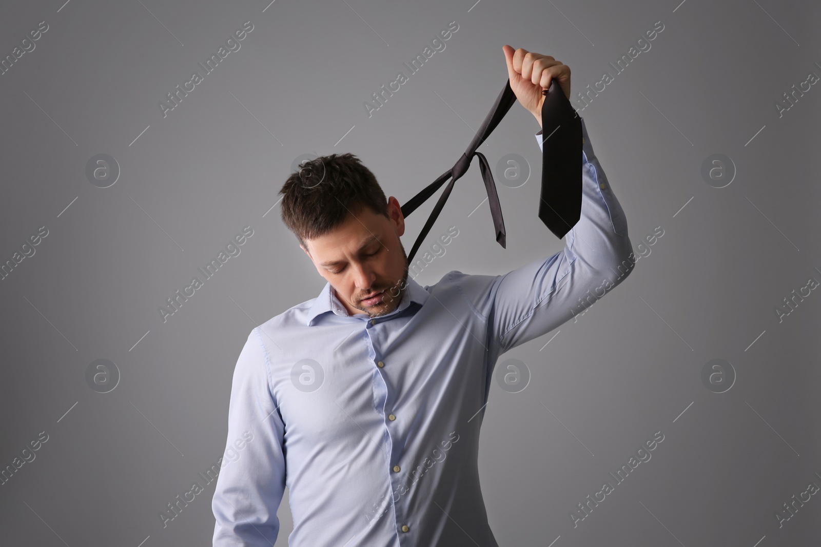 Photo of Depressed businessman holding tie like noose against light grey background