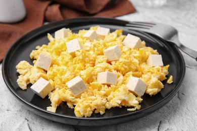 Plate with delicious scrambled eggs and tofu on white textured table, closeup