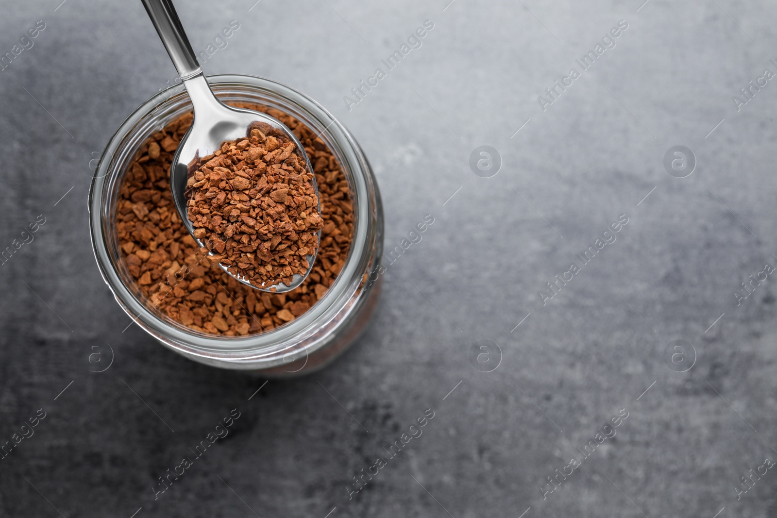 Photo of Instant coffee and spoon above glass jar on grey table, top view. Space for text