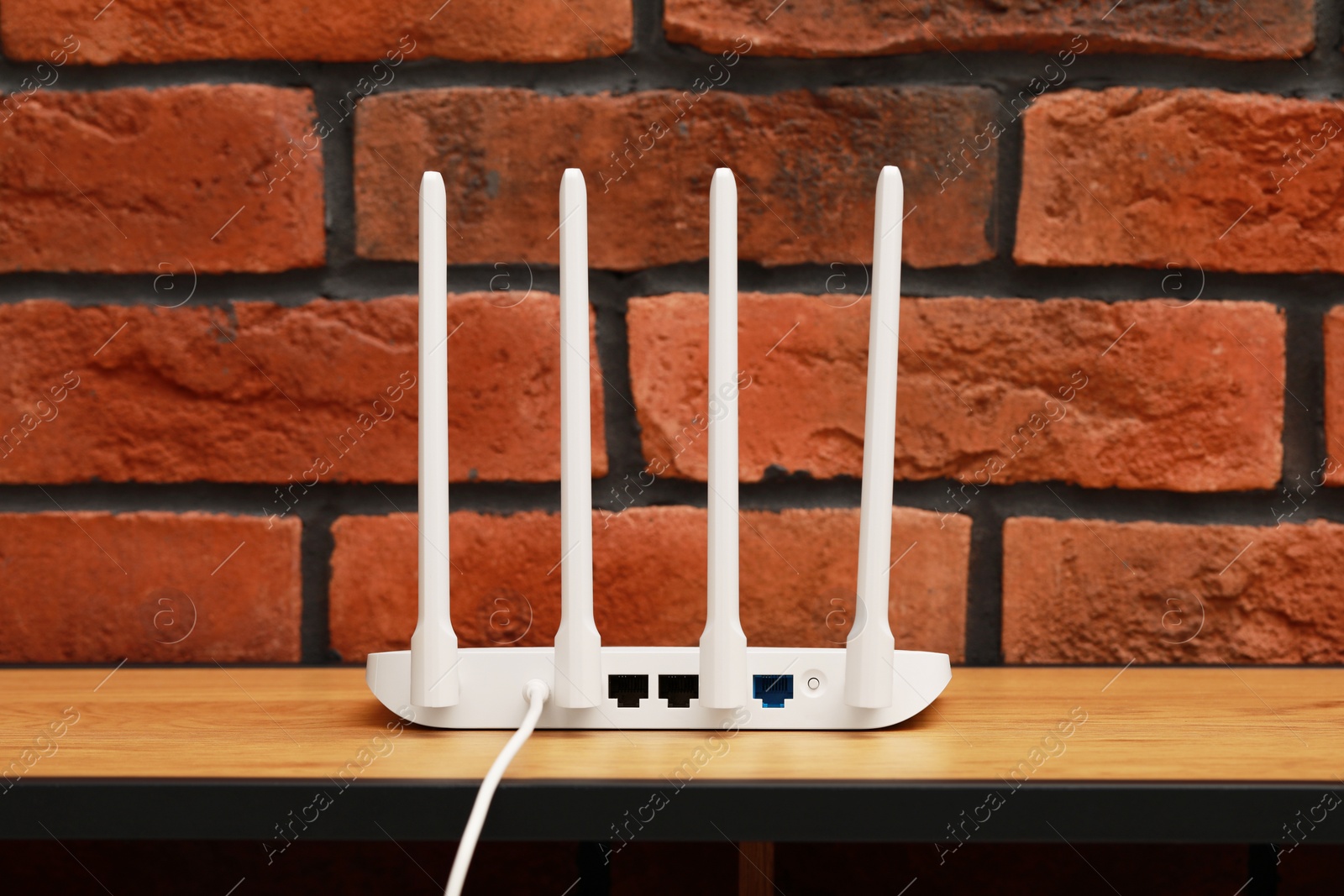Photo of New white Wi-Fi router on wooden table near brick wall