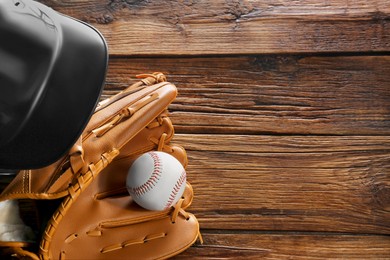 Photo of Baseball glove, batting helmet and ball on wooden table, flat lay. Space for text