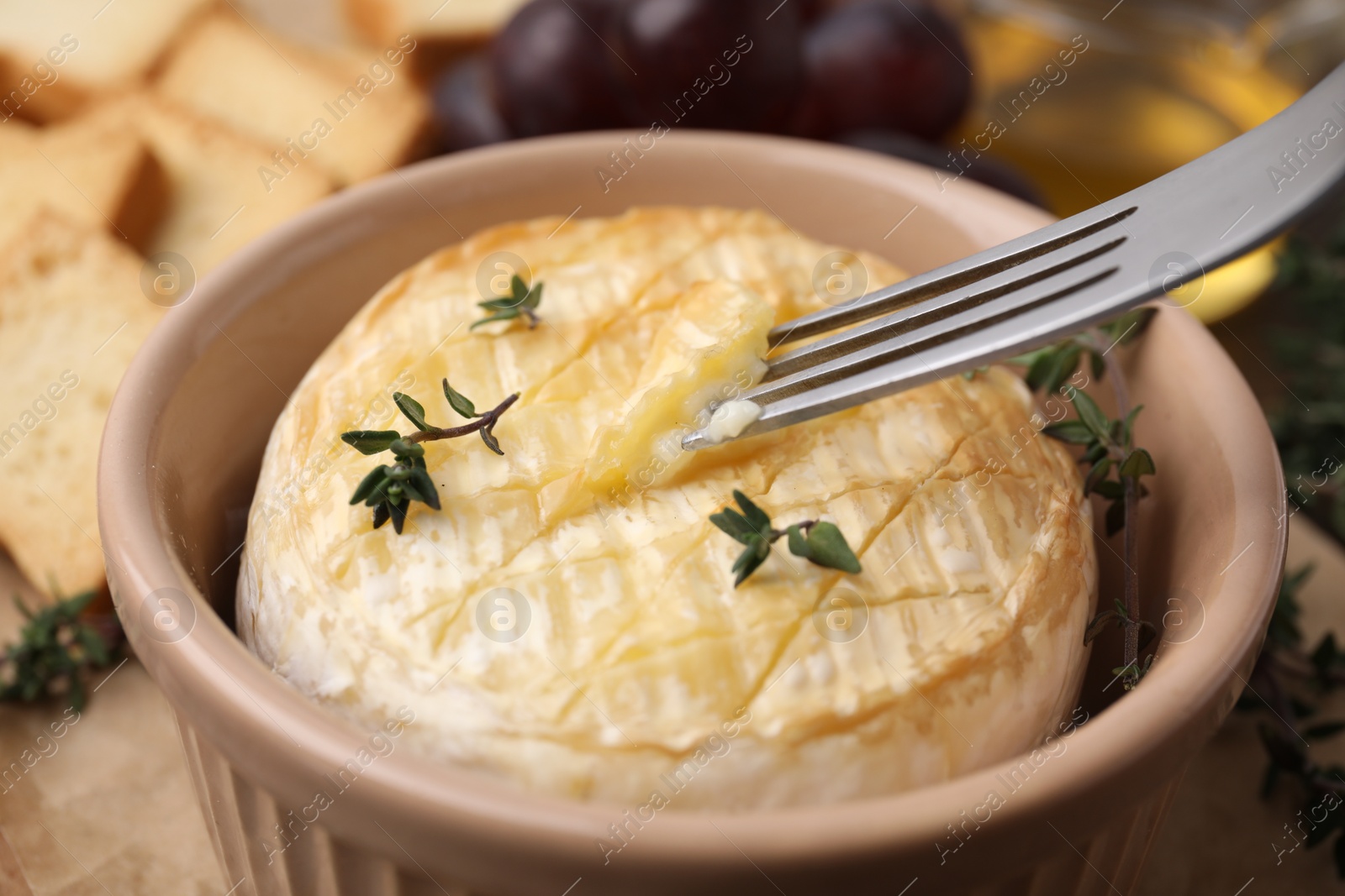 Photo of Taking tasty baked camembert with fork from bowl on table, closeup