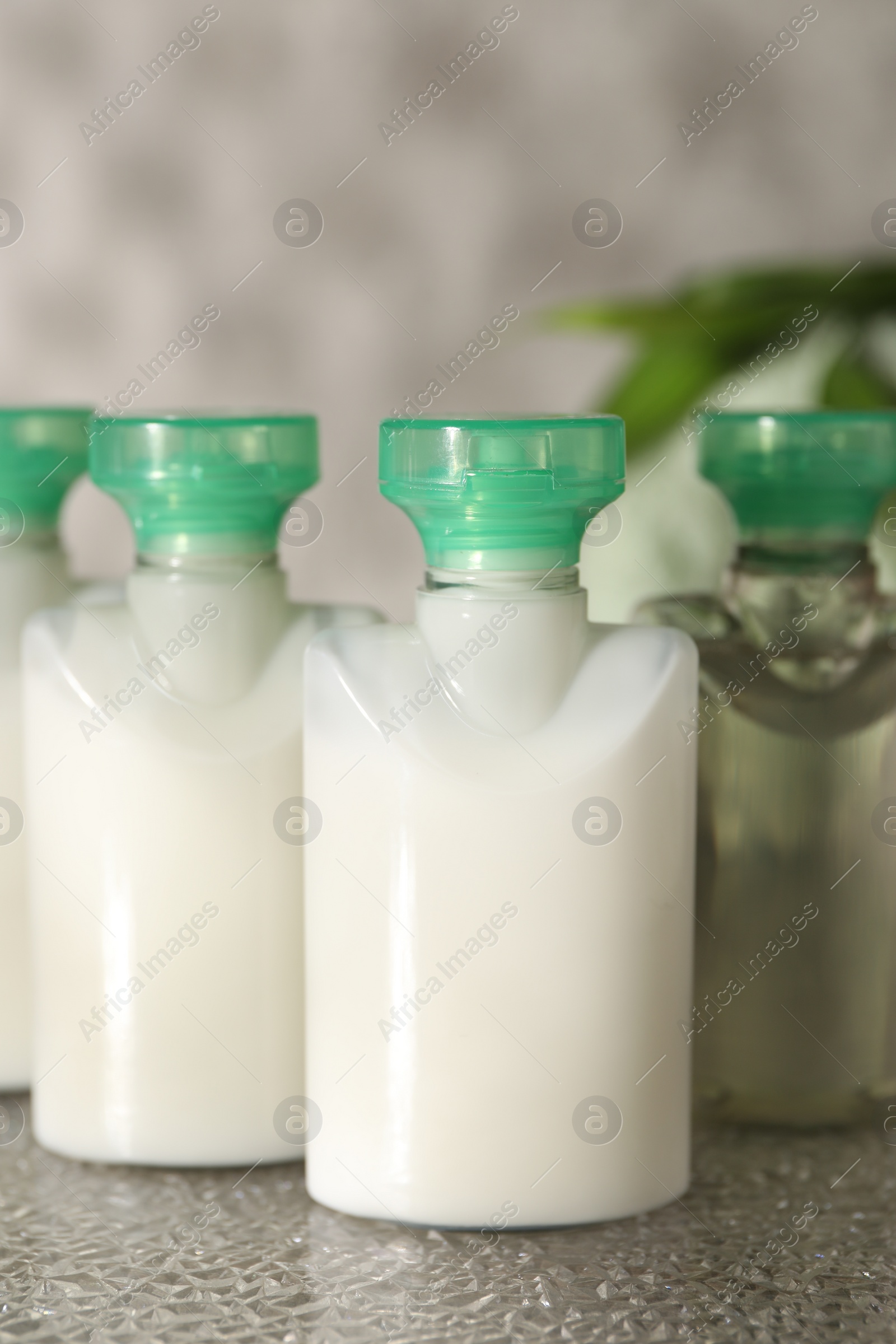 Photo of Mini bottles of cosmetic products on grey textured table, closeup