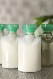 Mini bottles of cosmetic products on grey textured table, closeup