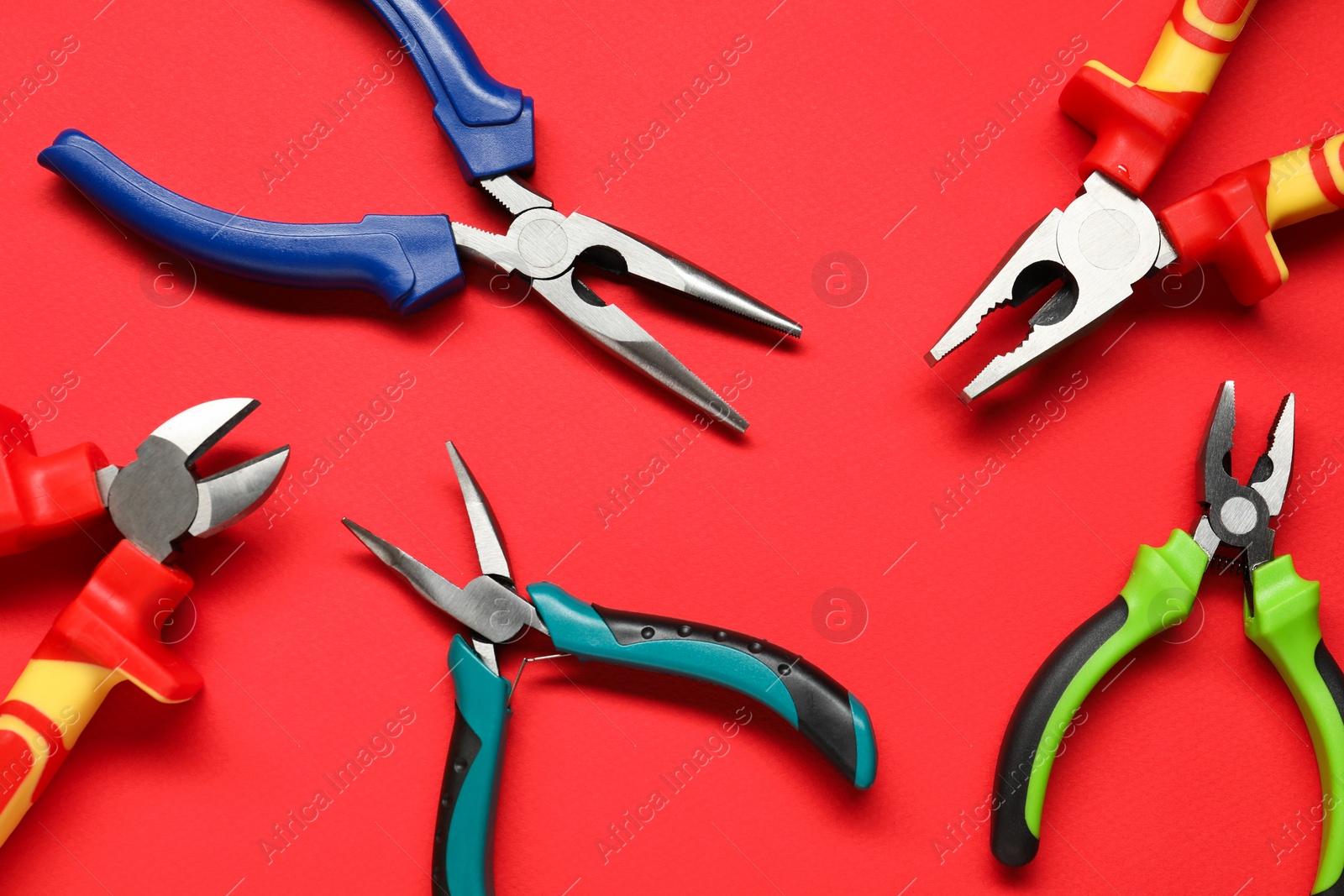 Photo of Different pliers on red background, flat lay