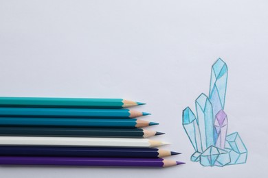 Photo of Drawing of crystals and colorful pencils on white background, top view