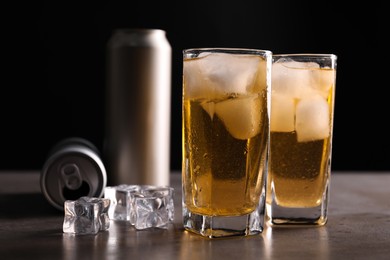 Photo of Energy drink in glasses, aluminium cans and ice cubes on grey table