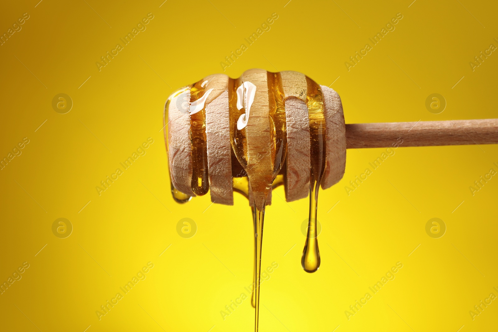 Photo of Delicious honey flowing down from dipper against yellow background, closeup