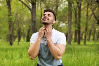 Young man scratching neck outdoors. Seasonal allergy