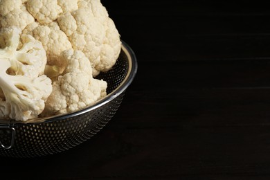 Photo of Colander with fresh raw cauliflower on black wooden table, closeup. Space for text