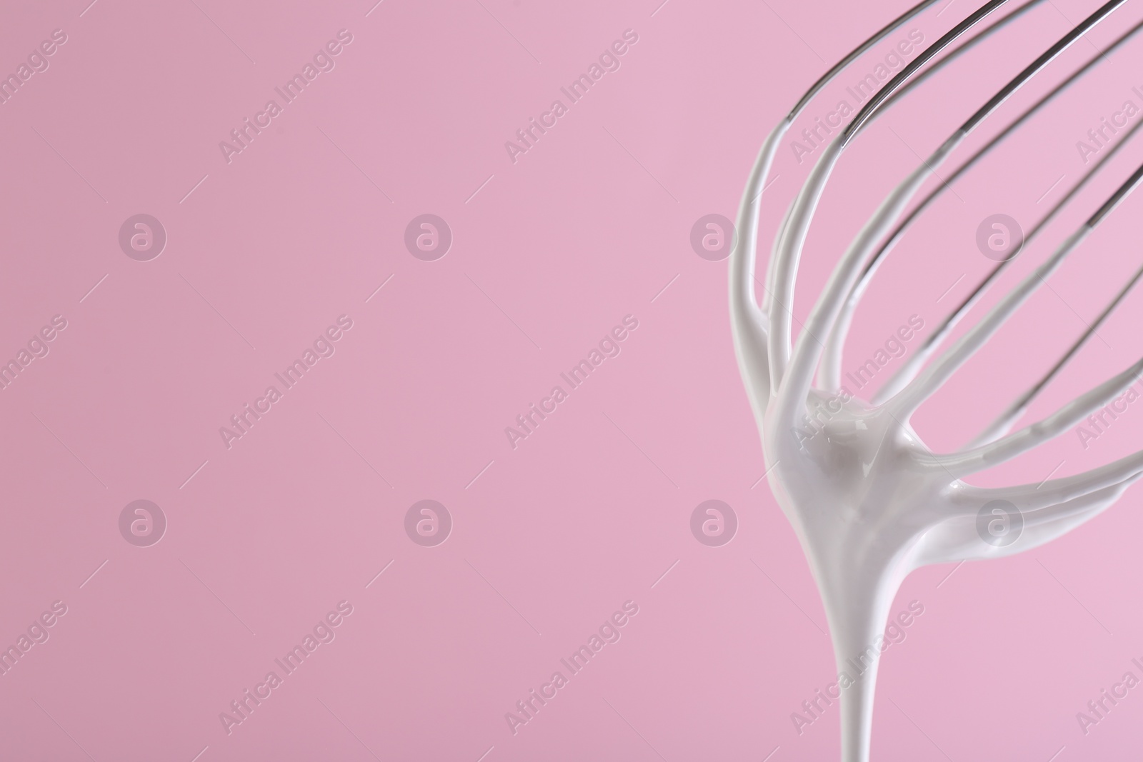 Photo of Whisk with whipped cream on pink background, closeup. Space for text