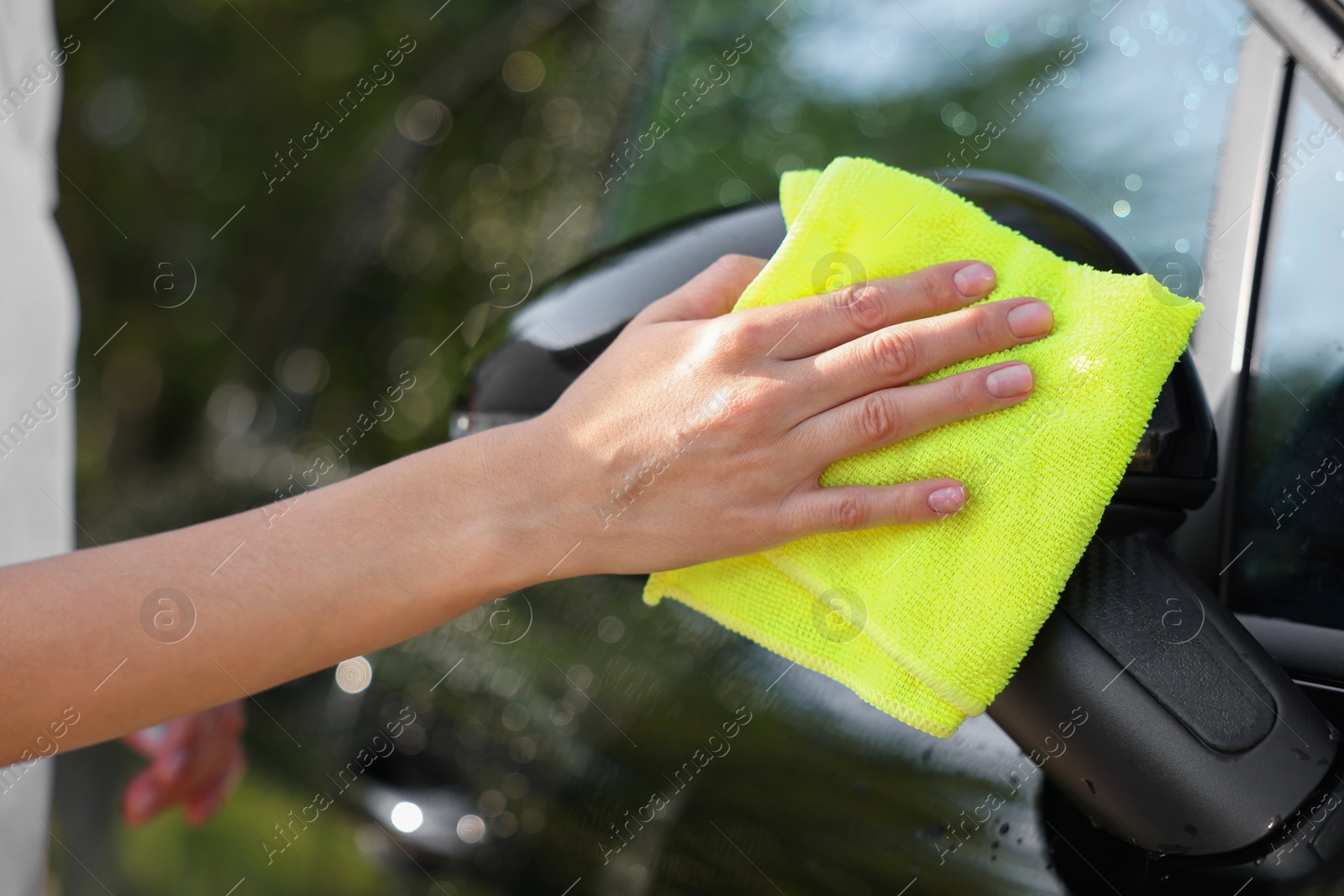 Photo of Woman washing car mirror with rag outdoors, closeup