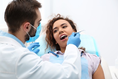 Dentist examining African-American woman's teeth with probe in hospital