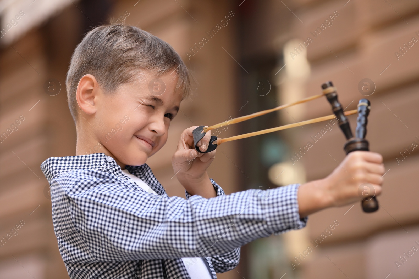 Photo of Little boy playing with slingshot outdoors on city street