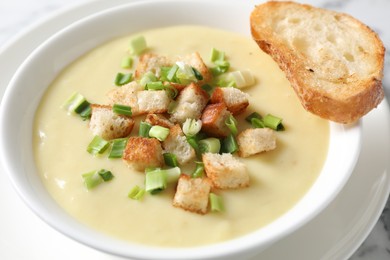 Photo of Tasty potato soup with croutons and green onion in bowl on white table