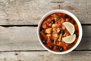 Meat solyanka soup with sausages, olives and vegetables in bowl on wooden table, top view. Space for text