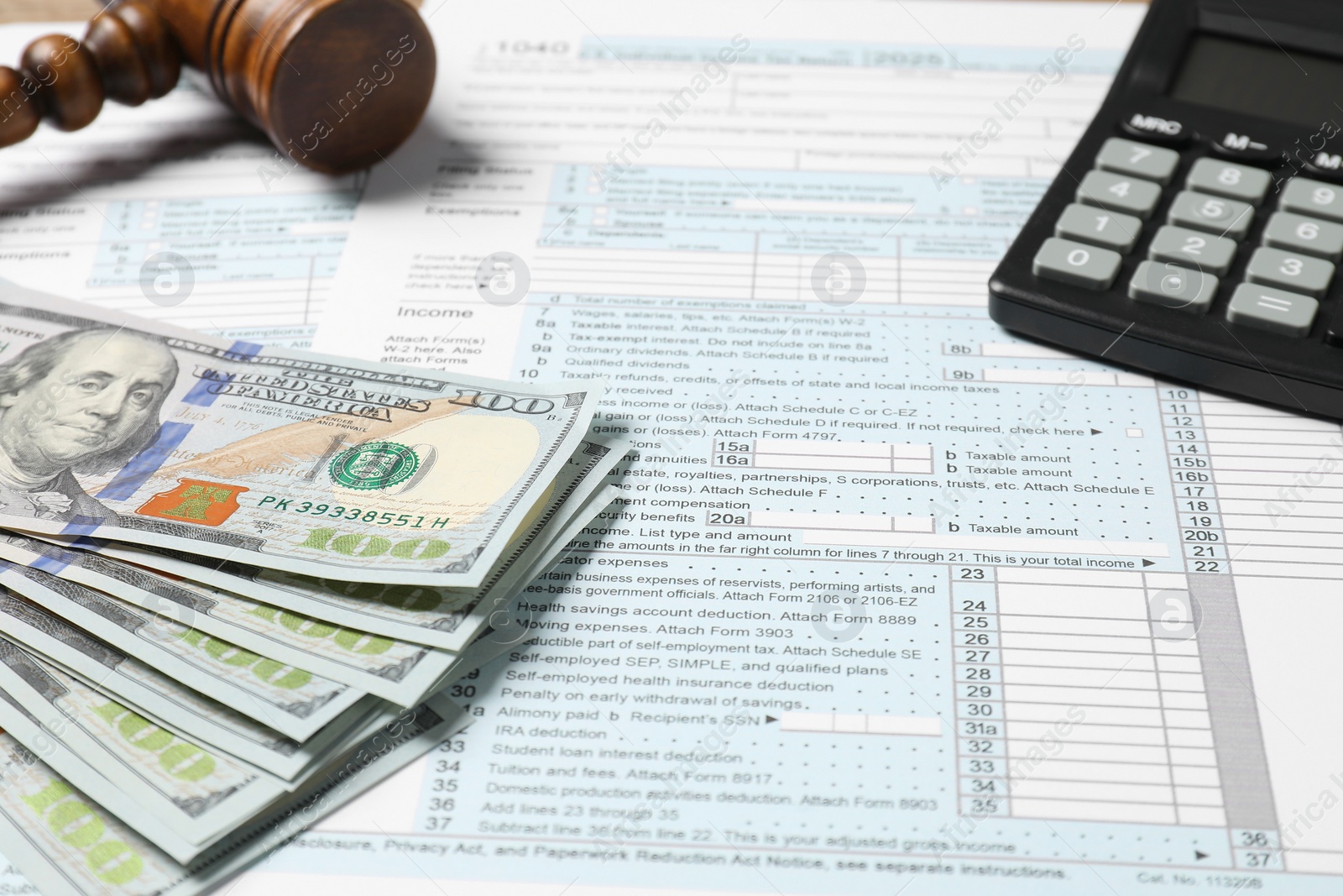 Photo of Tax return forms, dollar banknotes, calculator and gavel on table, closeup