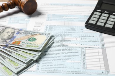 Tax return forms, dollar banknotes, calculator and gavel on table, closeup