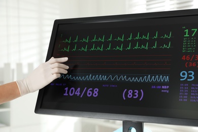 Nurse near monitor with cardiogram in hospital, closeup