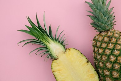Whole and cut ripe pineapples on pink background, flat lay