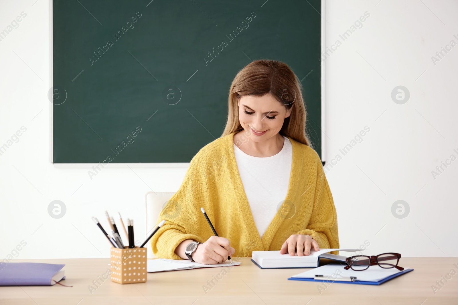 Photo of Young female teacher working at table in classroom