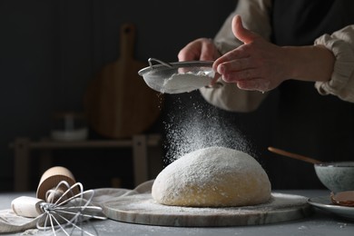Photo of Making dough. Woman sifting flour at grey table, closeup