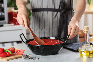 Woman cooking delicious tomato sauce in pan at table, closeup