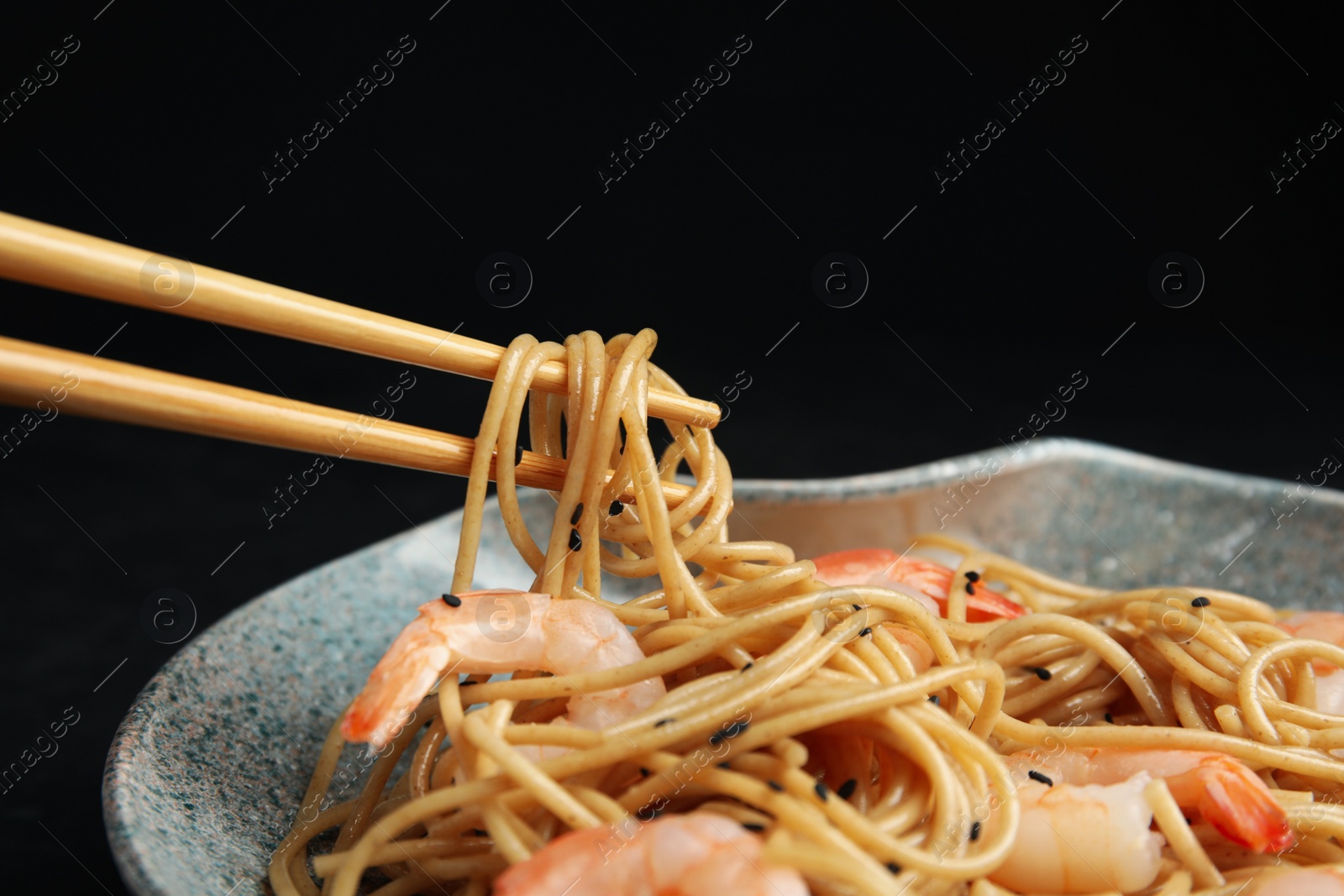 Photo of Chopsticks with tasty buckwheat noodles on black background, closeup