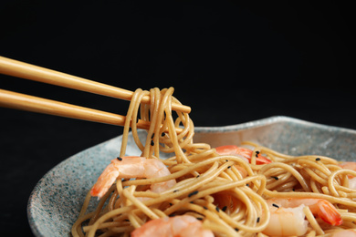 Photo of Chopsticks with tasty buckwheat noodles on black background, closeup