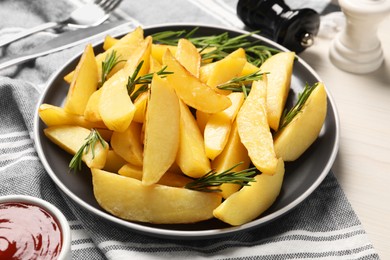 Photo of Plate with tasty baked potato wedges and rosemary on white wooden table, closeup