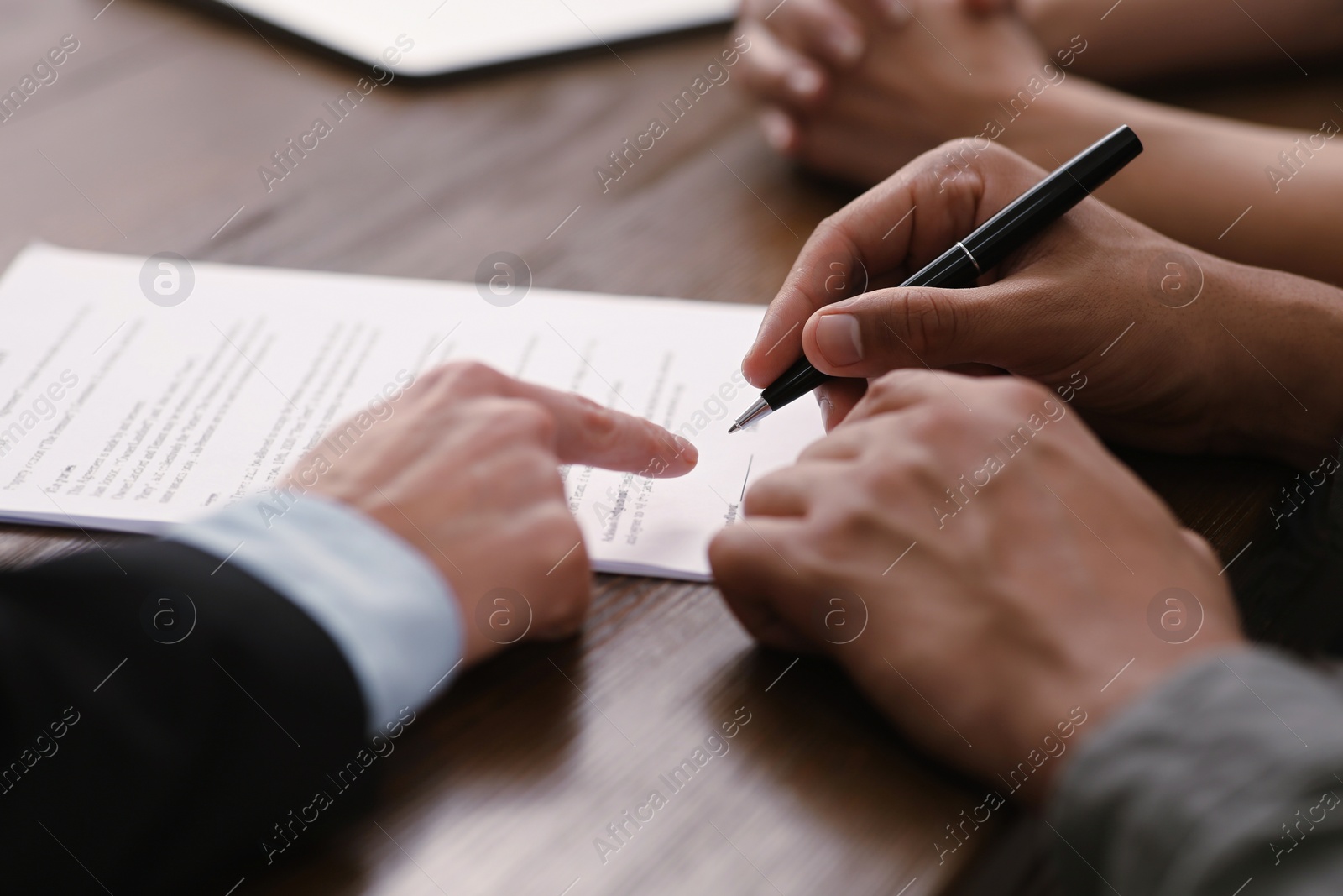 Photo of Notary helping couple with paperwork at wooden table, closeup